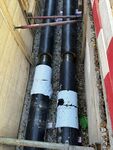 Ausbau des Wiener Fernkältenetzes Zwei nebeneinander liegende schwarze Rohre in einer Baugrube, an denen helle Isolierungen mit Beschädigungen sichtbar sind